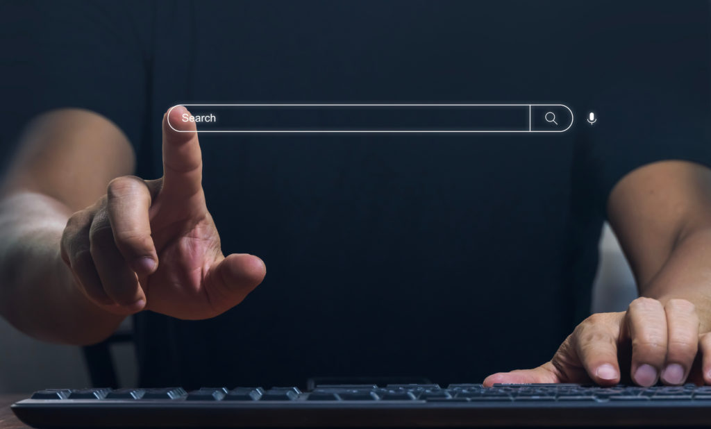 Man using a keyboard raising one hand in the air to touch a search bar in the air